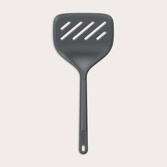 A Zyliss Turner XL slotted spatula in black, featuring a wide square head with three diagonal slots, ergonomic handle, and heat-resistant design is displayed against a plain light background. 