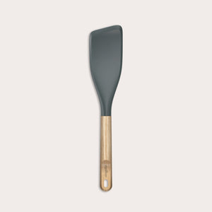 The Zyliss Oak Wood Easy Lift Turner has a dark gray silicone head, an oak wood handle, and a hanging hole at the end. It is shown on a plain light background.