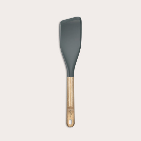 The Zyliss Oak Wood Easy Lift Turner has a dark gray silicone head, an oak wood handle, and a hanging hole at the end. It is shown on a plain light background.