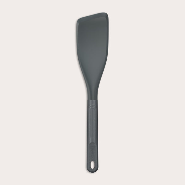 The Zyliss Easy Lift Turner is a gray, heat-resistant silicone utensil with a rectangular, angled head and long handle with hanging hole—perfect for non-stick cookware. Shown on a plain white background. 