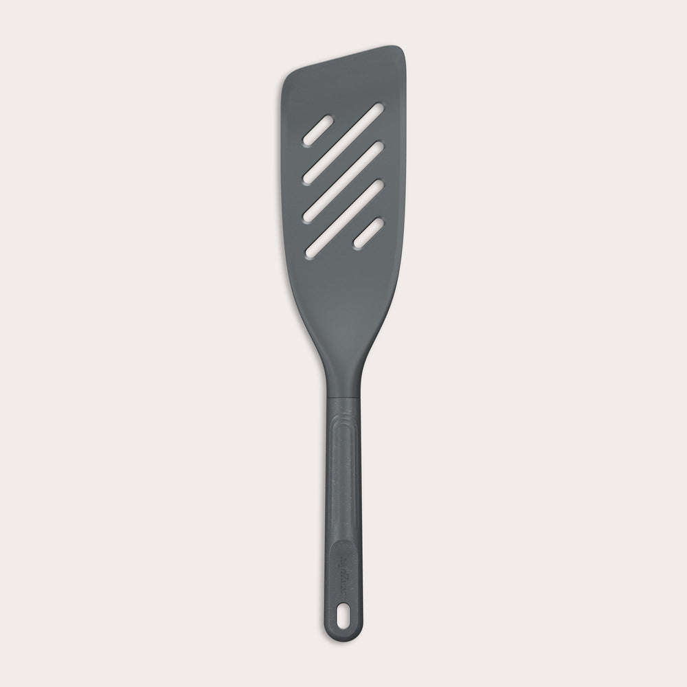 The Zyliss Fish Turner is a dark gray, heat-resistant slotted spatula with an angled edge and a handle featuring a hole at the end, displayed on a plain white background. 