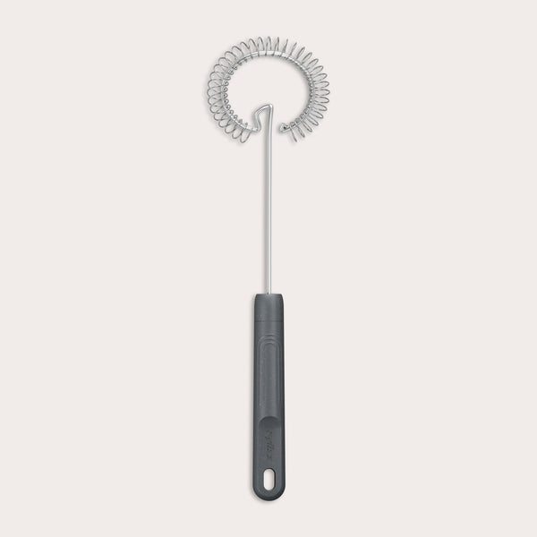 The Zyliss Gravy Whisk features a metal spiral and a dark plastic handle with a hanging hole. It is heat-resistant and shown against a plain light background. 