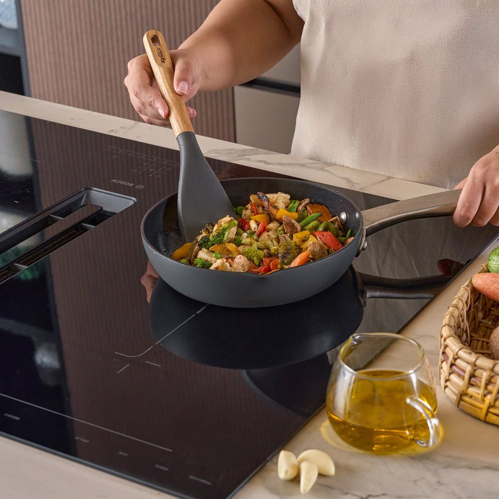 The Zyliss Oak Wood Easy Lift Turner has a dark gray silicone head, an oak wood handle, and a hanging hole at the end. It is shown on a plain light background.