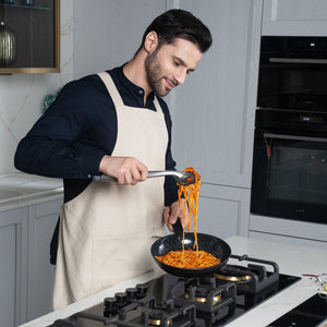 #24cm/9½"
A man in a beige apron cooks spaghetti with tongs in a Zyliss Ultimate Ceramic Fry Pan on a gas stove, focused and smiling slightly in a modern kitchen.