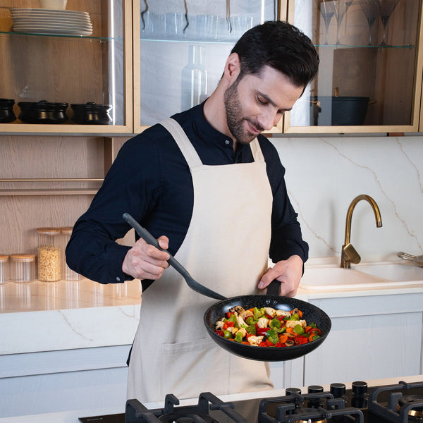 #28cm/11"
A man in a beige apron cooks a vibrant vegetable stir-fry in the Zyliss Ultimate Ceramic Fry Pan on a modern kitchen stove, smiling as he stirs and looks at the food.