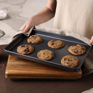A person holds a tray of cookies fresh from the oven, perfectly baked on the Zyliss Non-Stick Baking Tray for even heat distribution.