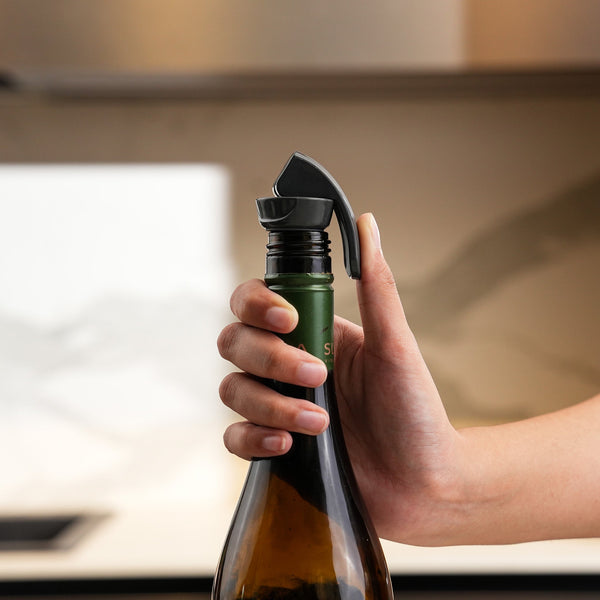 A hand presses a wine bottle onto the Zyliss Bottle Stopper 2 Piece Set in a kitchen, showing efficient drink storage with the black reusable stopper attached to the bottle’s neck.