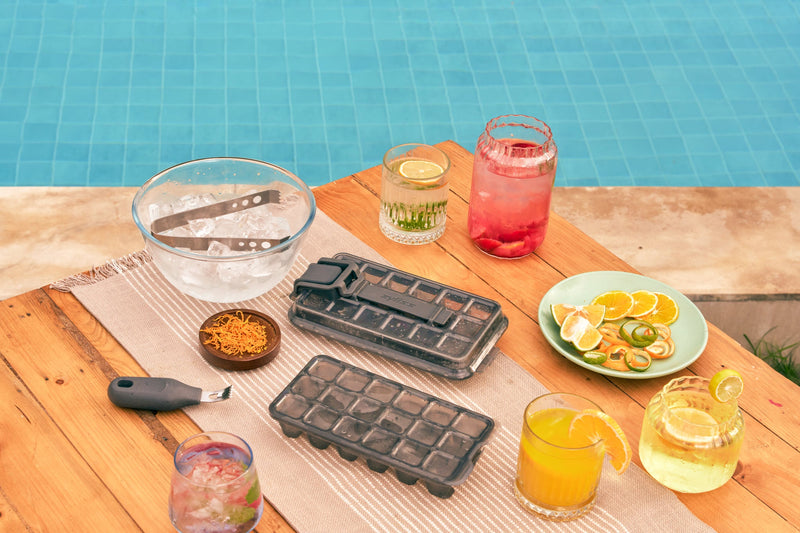 Two Zyliss Press & Pull ice cube trays beside fruit and drinks at a poolside table