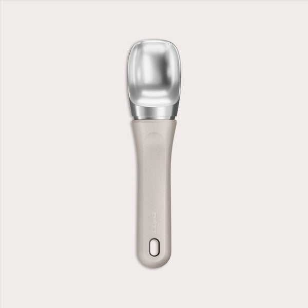 #naturalbeige The Zyliss Ice Cream Scoop features a wide, flat silver scoop and an eco-friendly beige handle made from sustainable wheat straw, with a small hole near the end, shown centered on a plain light background.