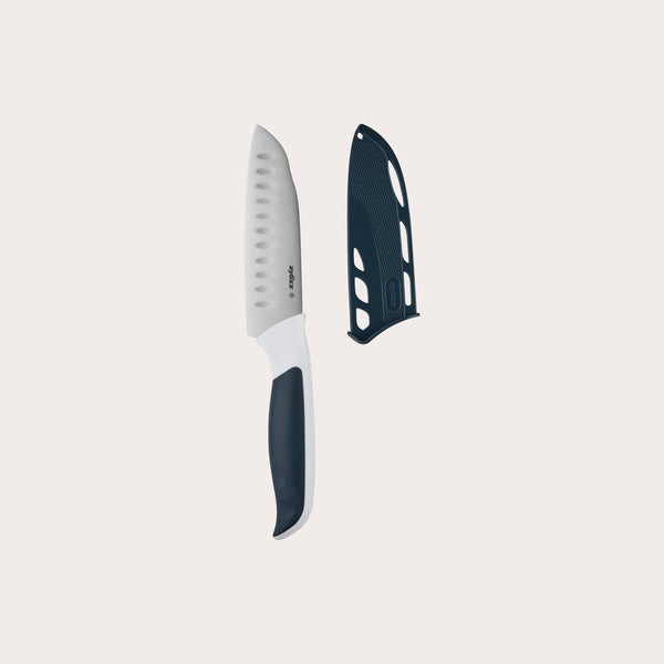 A Zyliss Comfort Mini Santoku Knife 12cm / 4¾ with a white and black ergonomic handle and matching black blade cover is placed beside it, set against a plain light background. 