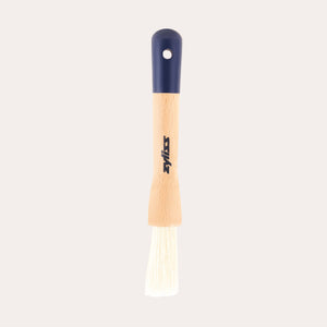 The Zyliss Beech Wood Pastry Brush features natural bristles, a beech wood handle with a printed logo, dark blue top, and hanging hole, shown on a plain white background. 