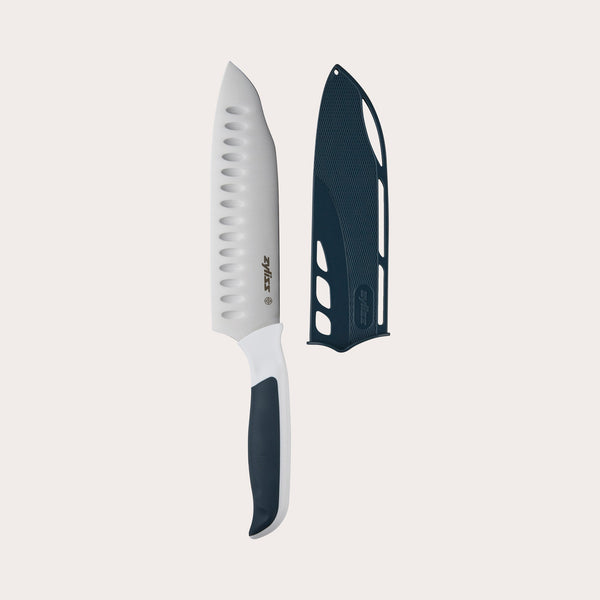 The Zyliss Comfort Santoku Knife 18cm/7 features a Japanese-inspired design with a white blade, black-and-white handle, and a black sheath, shown on a plain light background. 