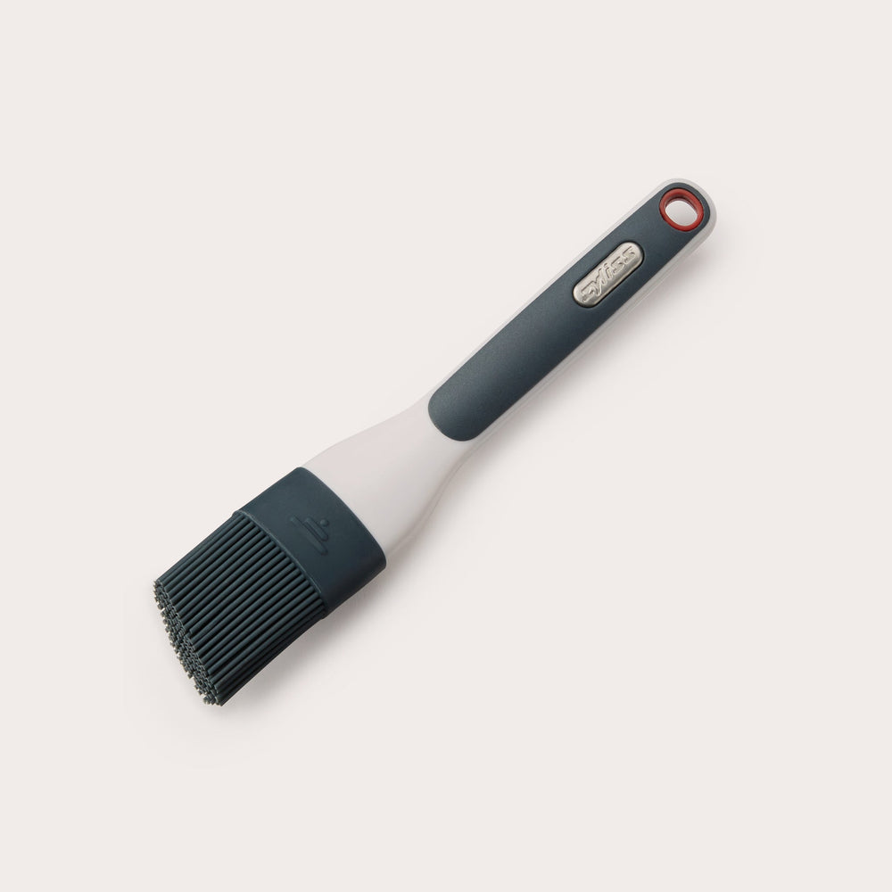The Zyliss Silicone Pastry Brush, available in black and white, features a long handle with a hanging hole and is dishwasher safe for easy cleaning. 