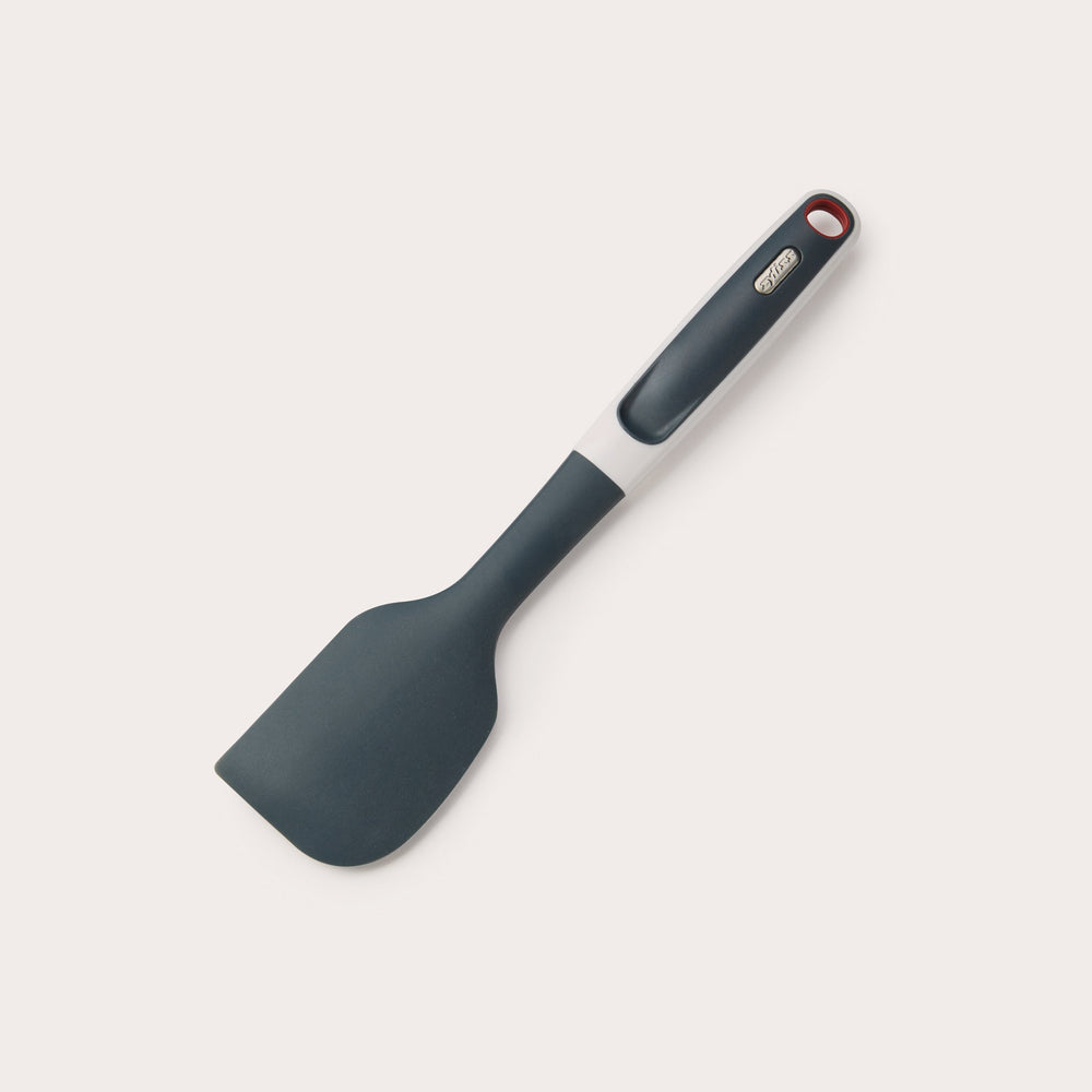 The Zyliss Does it All Silicone Spatula is black with a heat-resistant, ergonomic handle, a metal accent, and a hanging hole. Shown on a plain white background. 