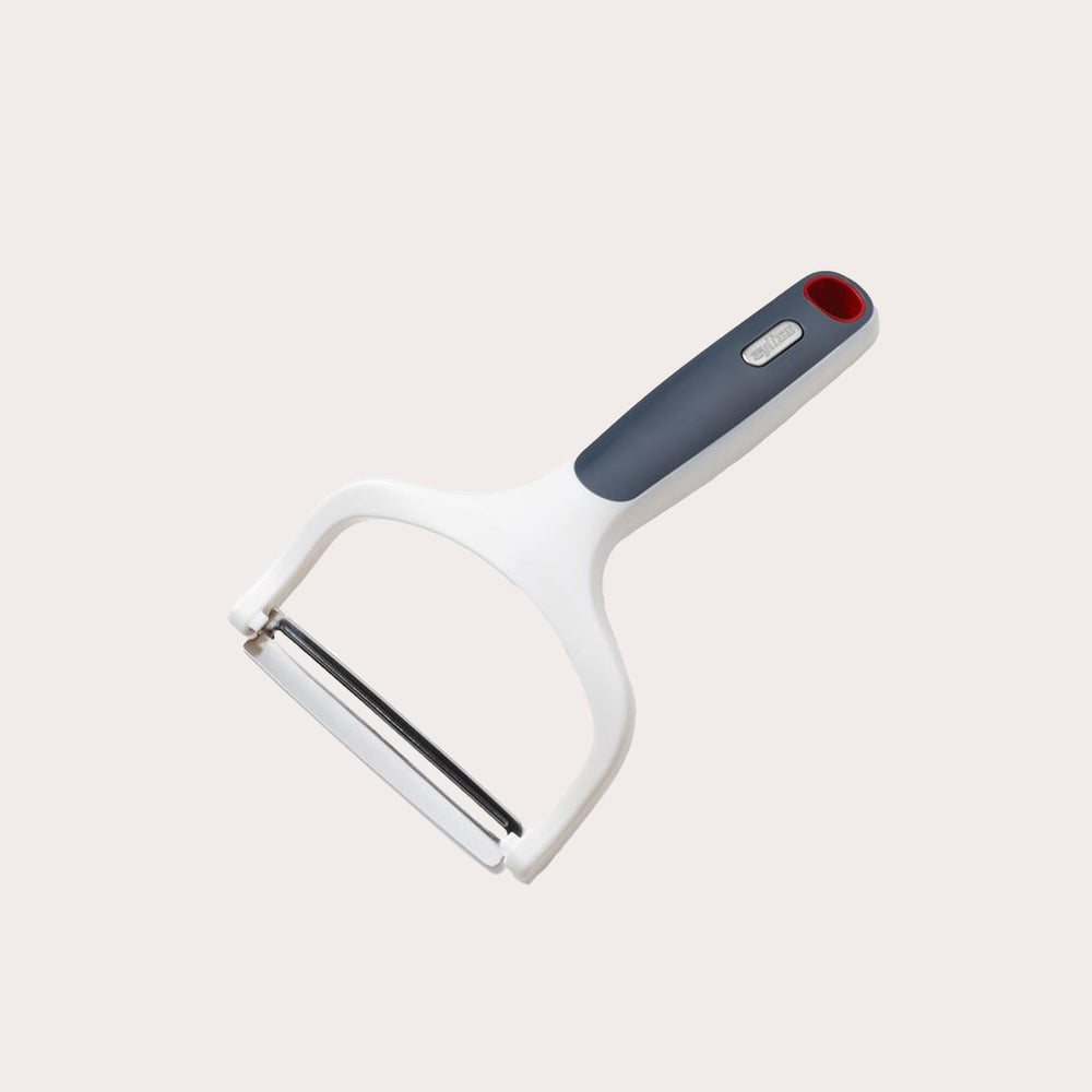 The Zyliss Smooth Glide Wide Peeler features a soft-touch white and gray handle with a red accent, a stainless steel blade, and is displayed on a plain light background. 