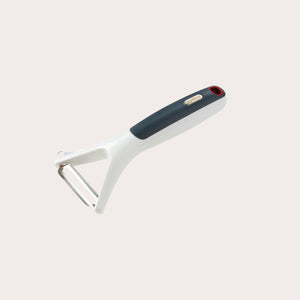 The Zyliss Smooth Glide Y-Peeler, with an ergonomic white and black handle and a sharp stainless steel blade, is shown on a plain light-colored background. 