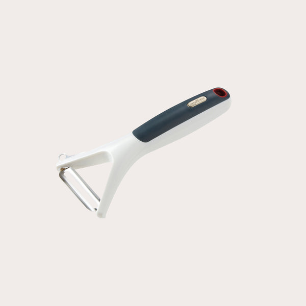 The Zyliss Smooth Glide Y-Peeler, with an ergonomic white and black handle and a sharp stainless steel blade, is shown on a plain light-colored background. 