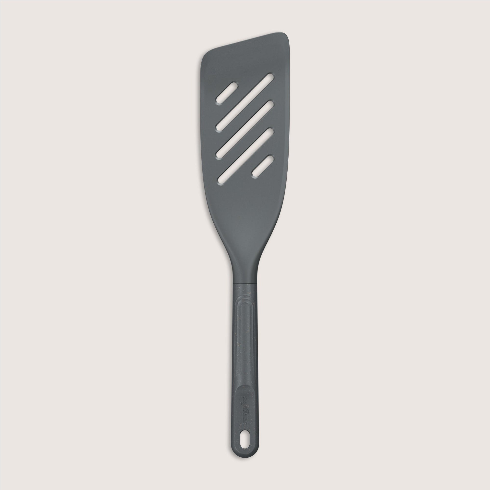 A dark gray slotted spatula with a long handle and four diagonal slots, photographed on a light background.