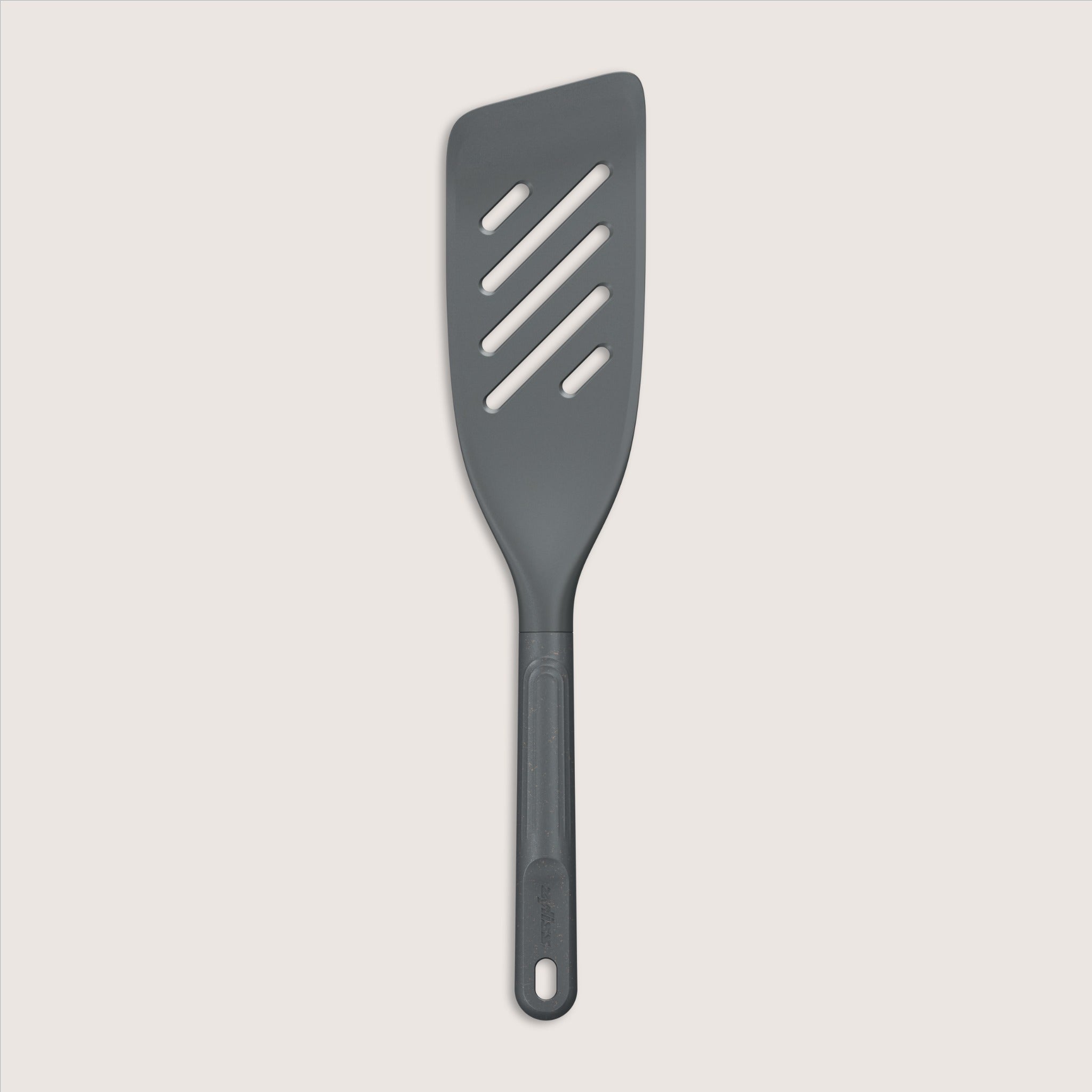 A dark gray slotted spatula with a long handle and four diagonal slots, photographed on a light background.