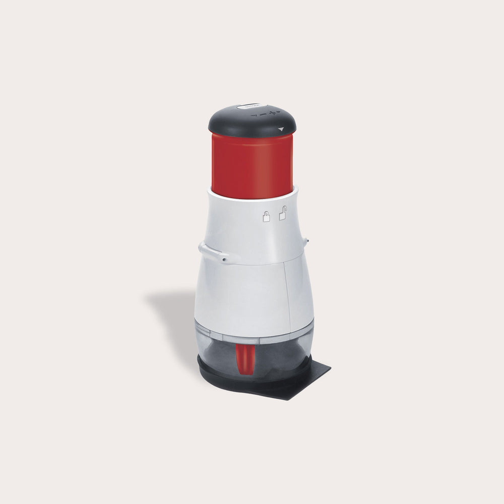 The Zyliss Zick-Zick 2 Food Chopper stands upright on a clear and black base, featuring a black top, red middle section, and white body, resembling a storage container against a plain light background. 