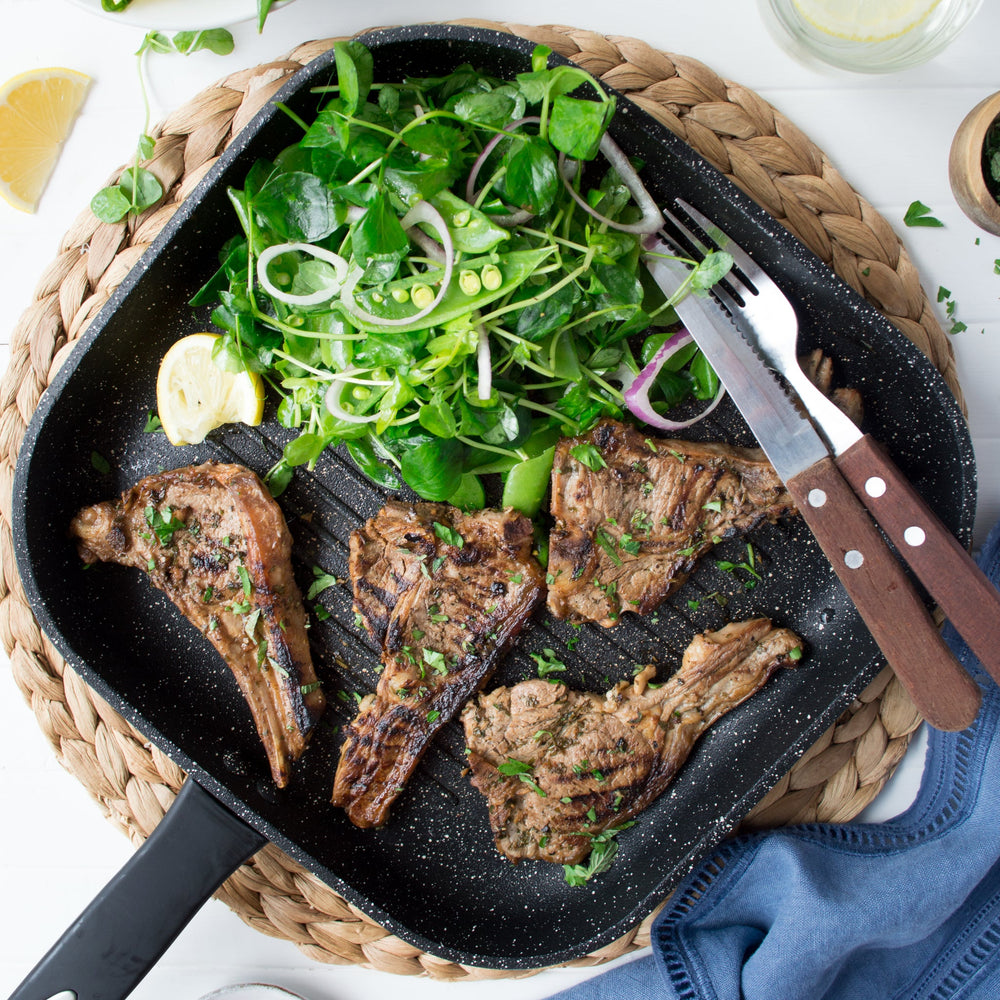 The Zyliss Ultimate Non-Stick Grill Pan is black, square, and PFOA-free with Swiss non-stick coating, raised ridges, and a long handle. Shown on a plain light background. 