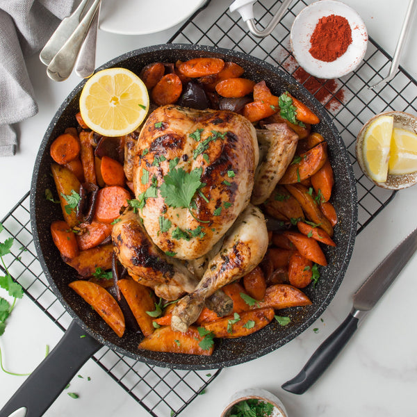 A roasted whole chicken garnished with cilantro sits in the Zyliss Ultimate Non-Stick Frying Pan, surrounded by carrots and potatoes. Lemon halves and paprika highlight its scratch-resistant, quality non-stick surface. #20cm/8"&28cm/11"