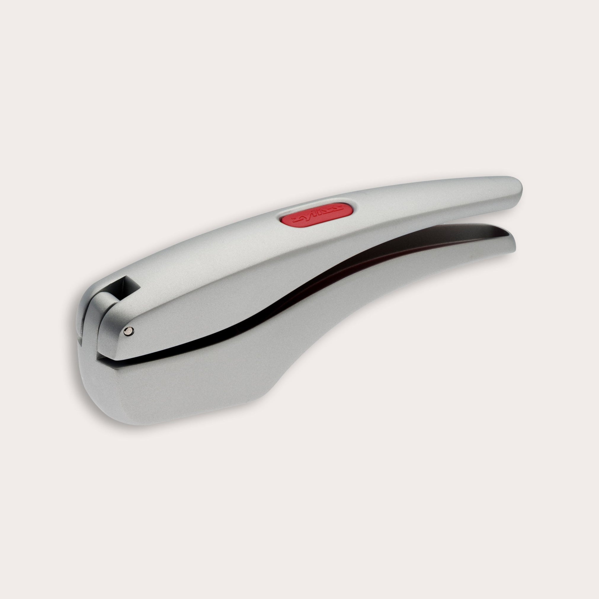 A silver metal garlic press with a sleek, curved design and a red button on top, shown against a plain light background.